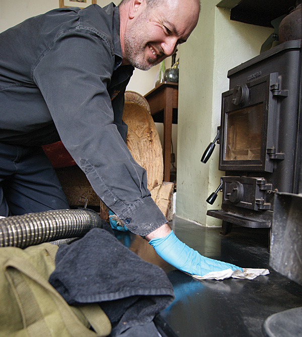 Les Bowering smiling as he wipes down a wood stove hearth, vacuum hose beside him