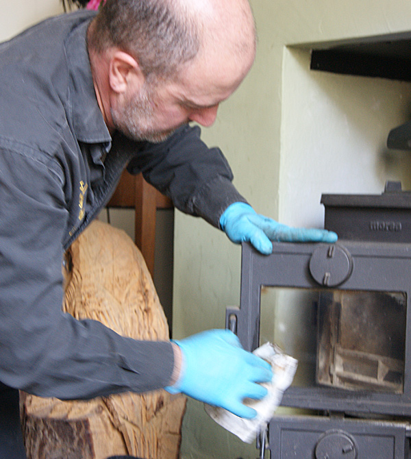 Les in blue gloves cleaning the glass and door of a wood stove