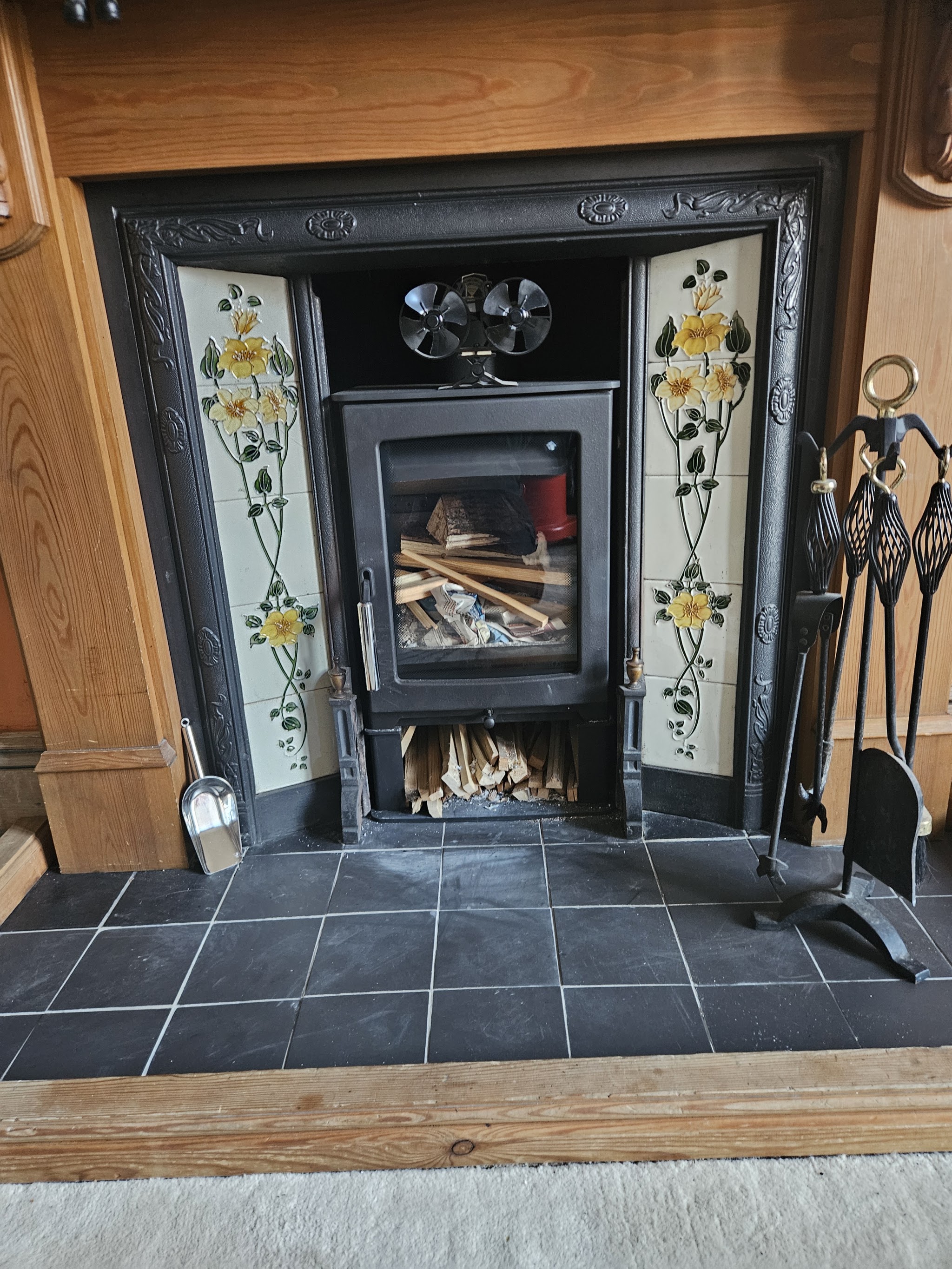 A clean wood-burning stove set in a tiled Victorian fireplace with a slate hearth